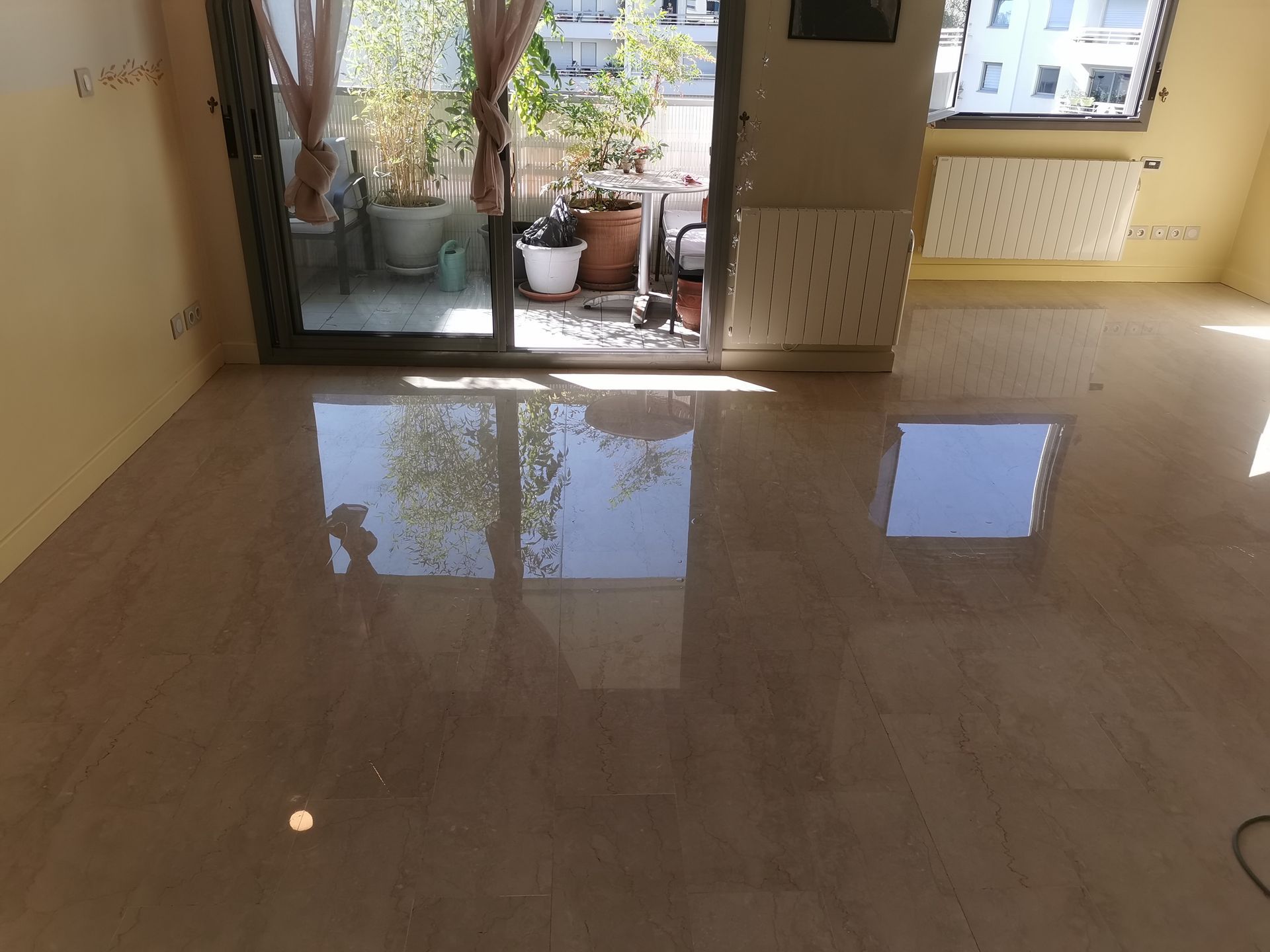 Un sol en marbre beige clair, poli et brillant, reflétant la lumière d'un balcon et d'une fenêtre dans une pièce vide.