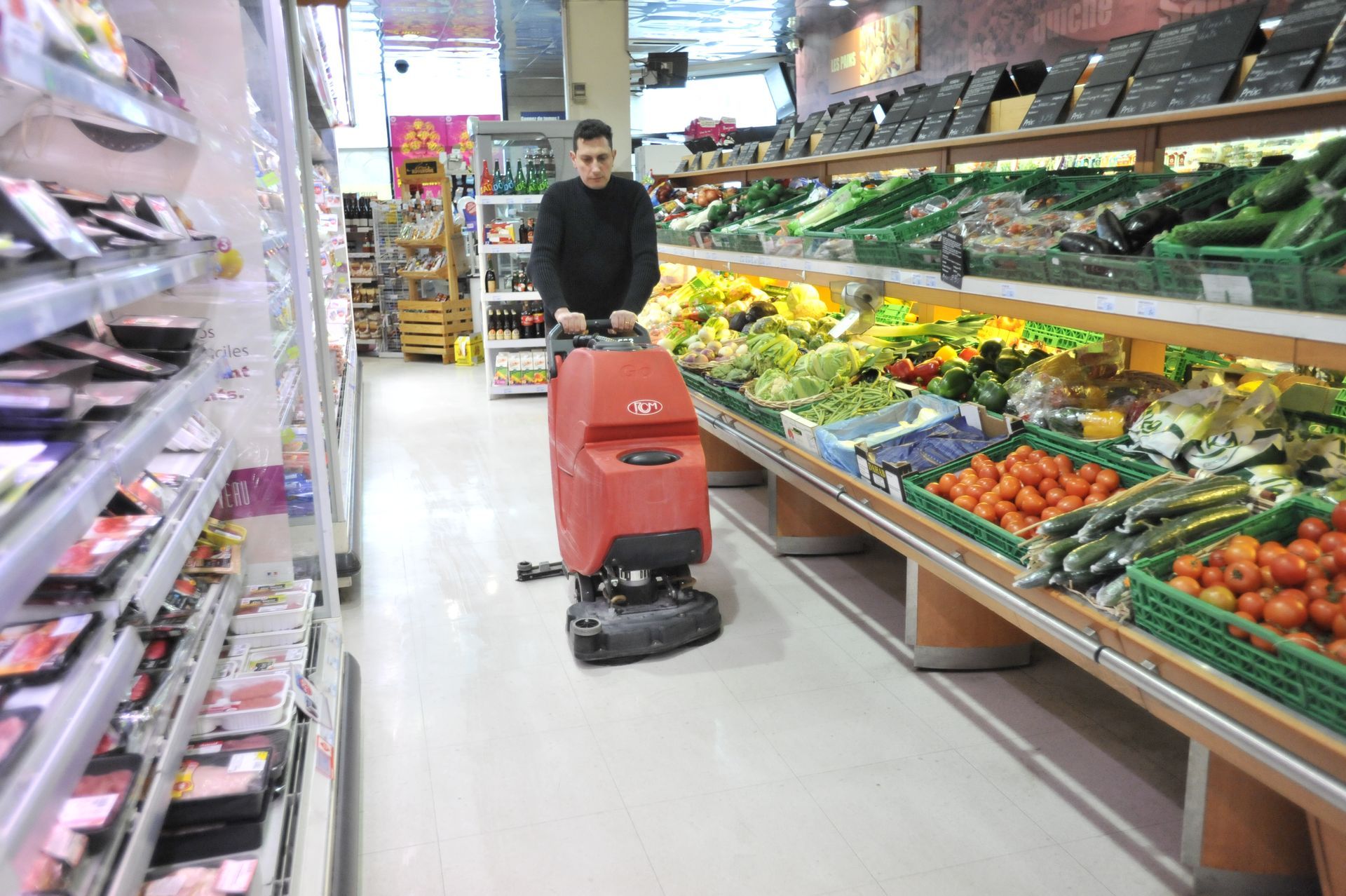 Nettoyage d'une allée de magasin avec une machine industrielle rouge.