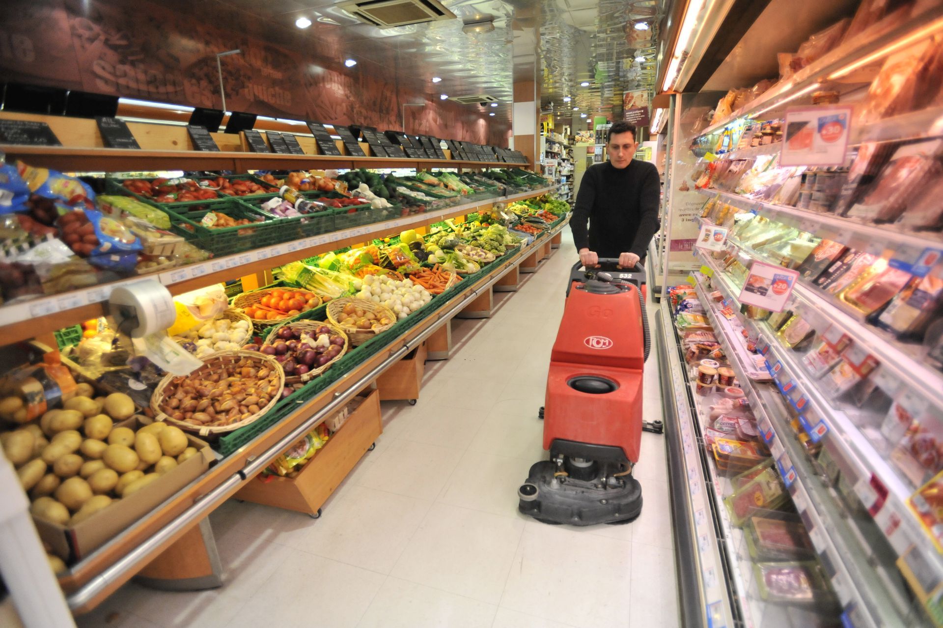 Un homme pousse une machine de nettoyage de sol industriel dans les allées d'un magasin.