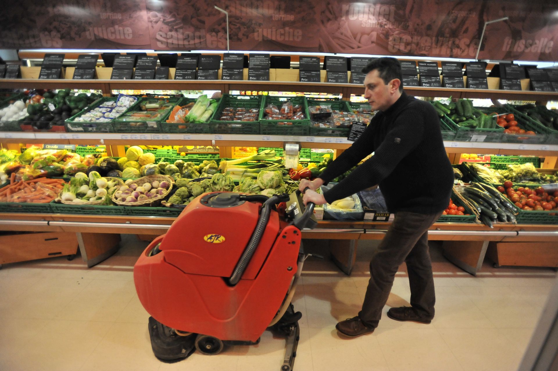 Un homme nettoie le sol d'un magasin dans le rayon fruits et légumes.