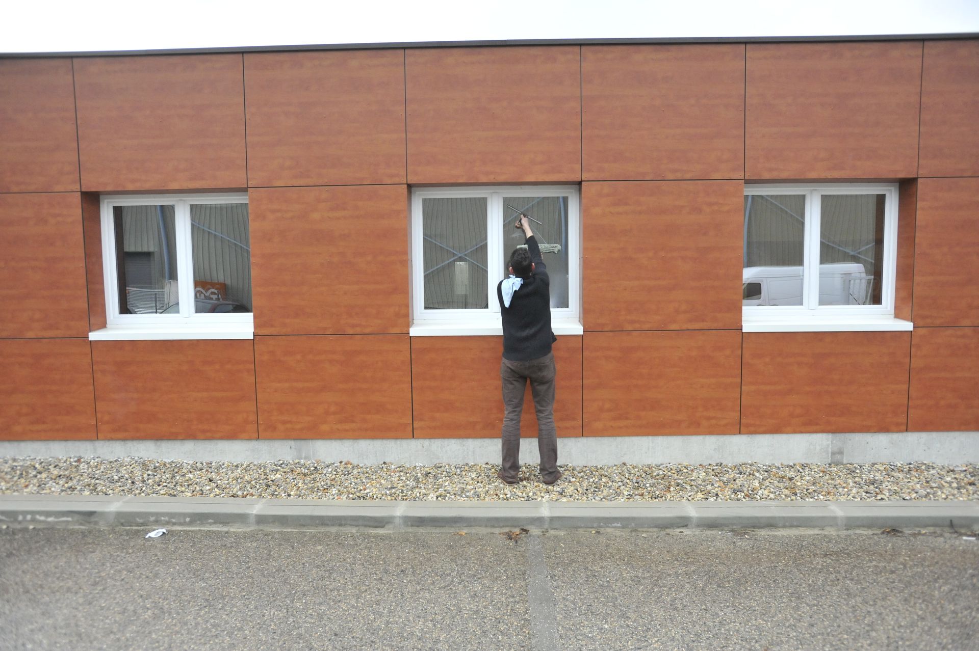Nettoyage de vitres en cours le long d'une façade marron.