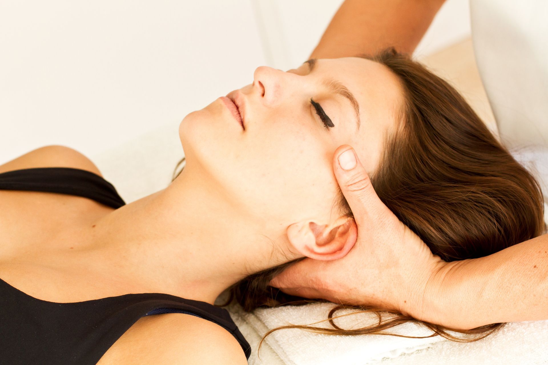 Femme recevant un massage du cou, allongée, les yeux fermés, fond blanc, gros plan.