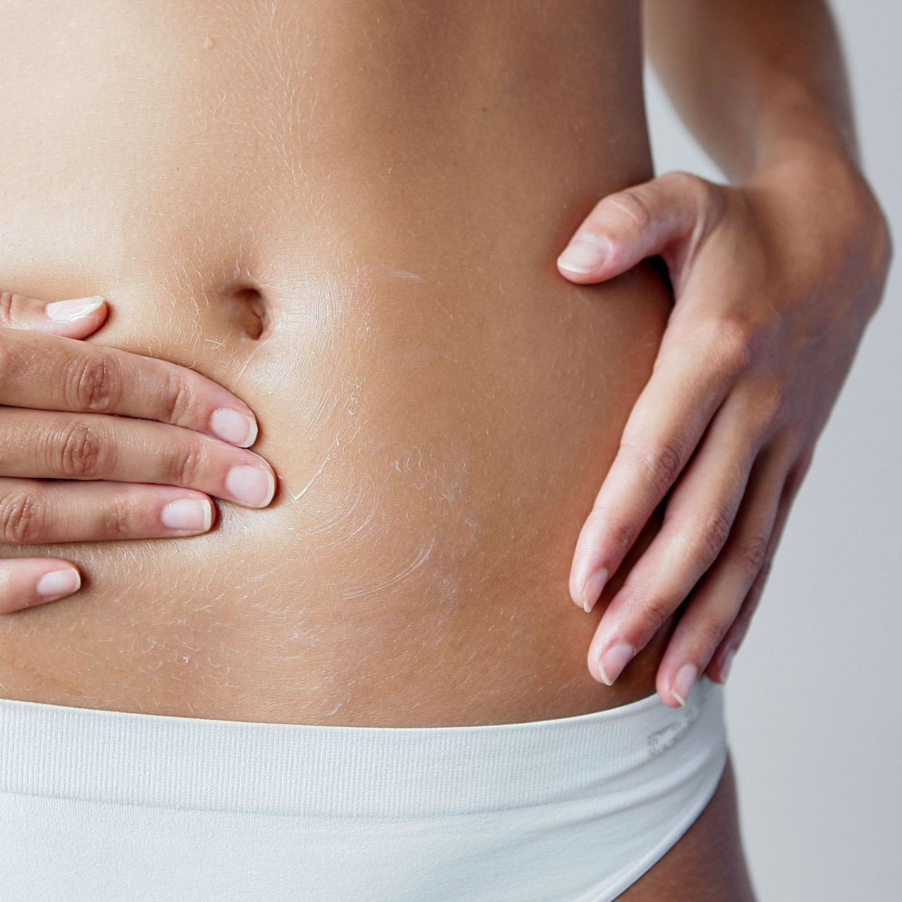 L'abdomen d'une personne, la main le touchant ; la peau luisante. Sous-vêtements blancs.