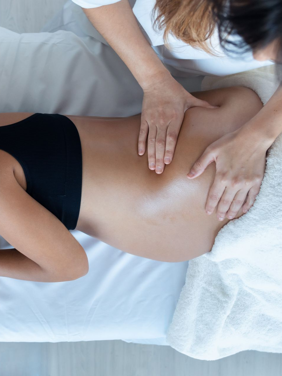 Une personne reçoit un massage du dos sur une table de massage. Le dos de la personne est massé avec les mains.