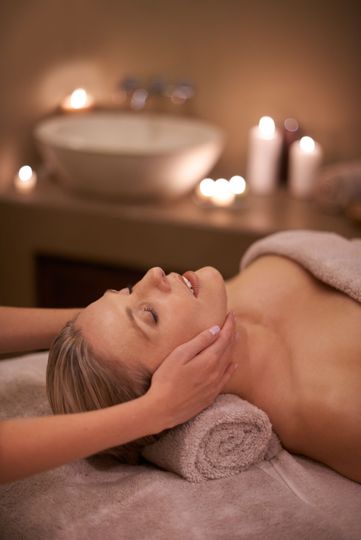 Femme recevant un soin du visage, allongée sur une table de massage. Bougies et lavabo en arrière-plan.