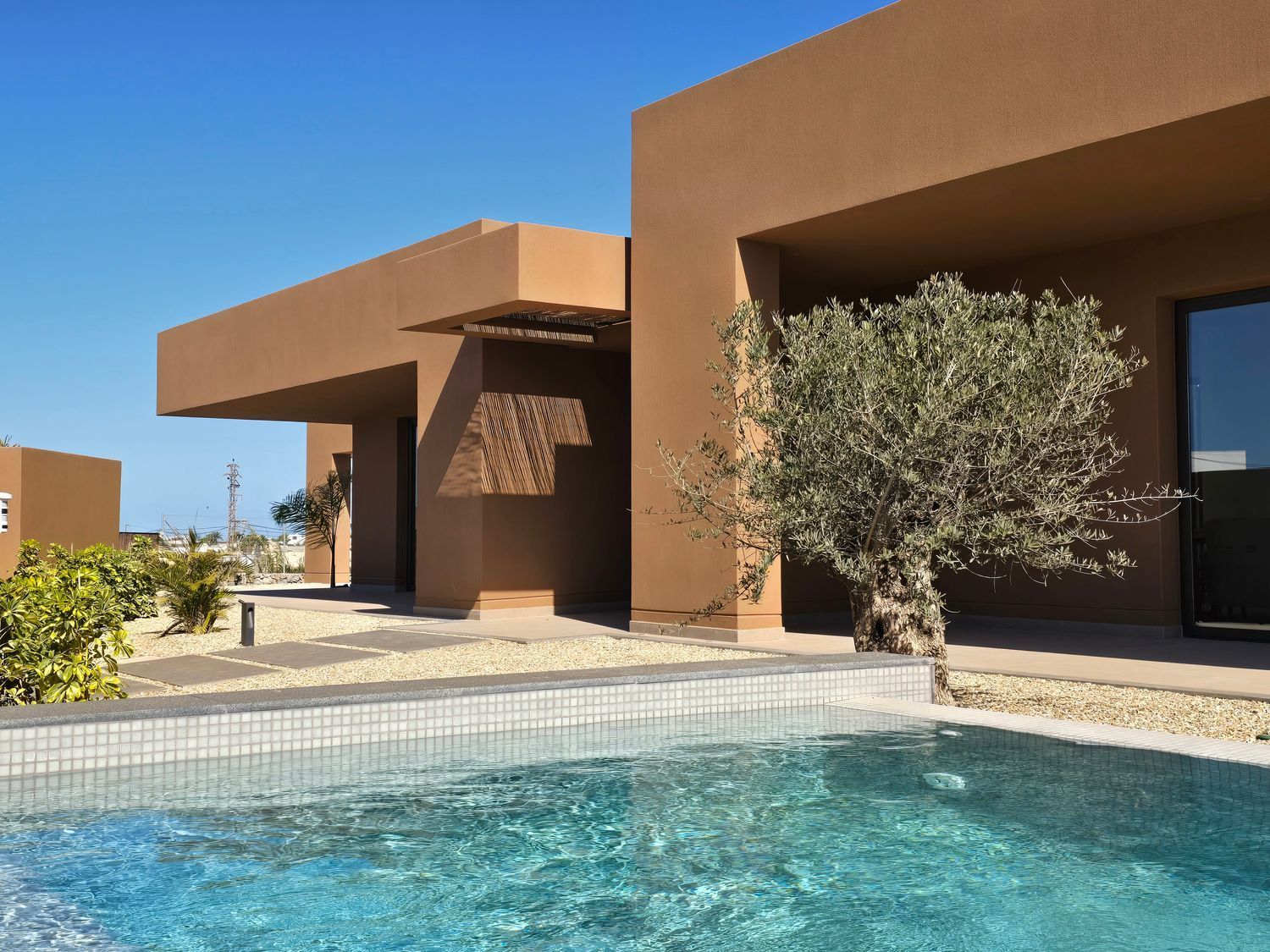 Casa moderna de estilo desértico con piscina turquesa y patio soleado.