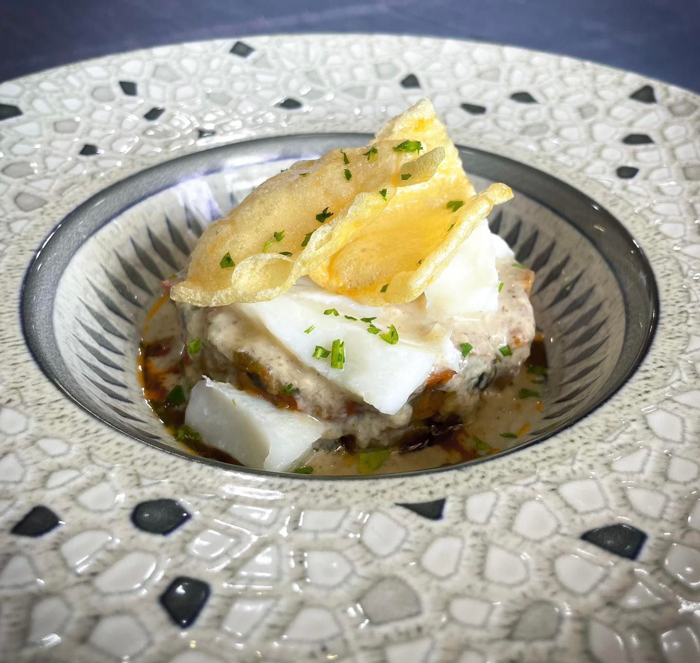 Pescado entero a la parrilla en un plato blanco, cubierto con hierbas verdes picadas y aceite.