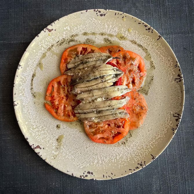 Pasta rellena servida en un plato, cubierta con salsa de tomate, carne en rodajas y espolvoreada con queso rallado.