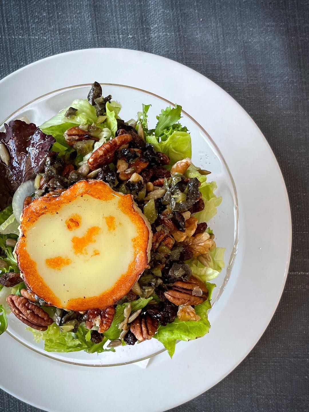 Ensalada coronada con un huevo frito redondo y nueces pecanas en un plato blanco.