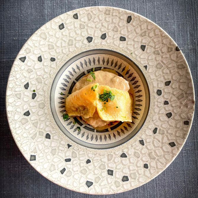 Pequeño pastelito emplatado con guarnición verde sobre una mesa blanca decorativa.