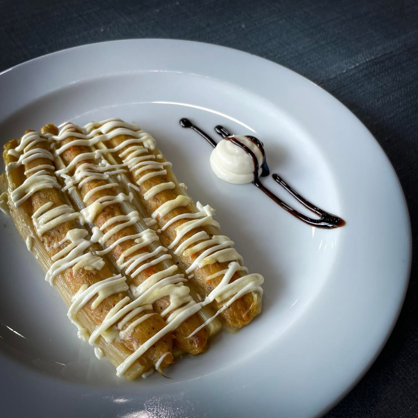Crepe de postre bañada en crema y caramelo, servida en un plato blanco con una bola de helado de vainilla.