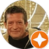 Hombre sonriente con camisa oscura sobre fondo dorado y un icono de estrella en la esquina.