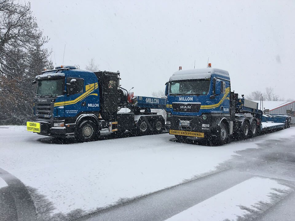 Deux semi-remorques bleues arborant des marquages ​​jaunes sont garées côte à côte sur un sol enneigé par une journée d'hiver.
