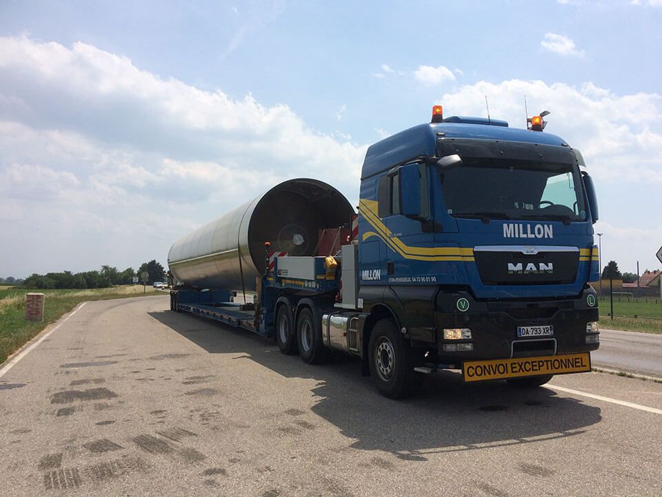 Un semi-remorque MAN bleu, portant le logo Villon à l'avant, transporte un gros cylindre industriel sur une remorque ouverte, sur une route.