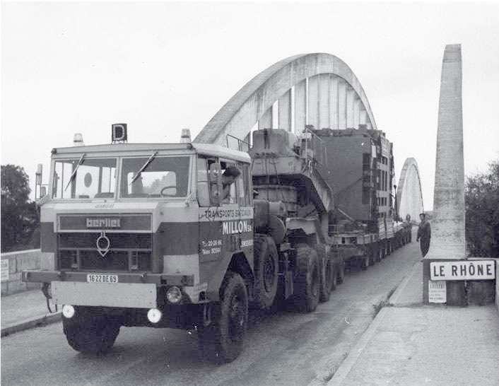 Un camion Berliet transportant une importante charge industrielle sur un pont en arc de béton enjambant le Rhône.