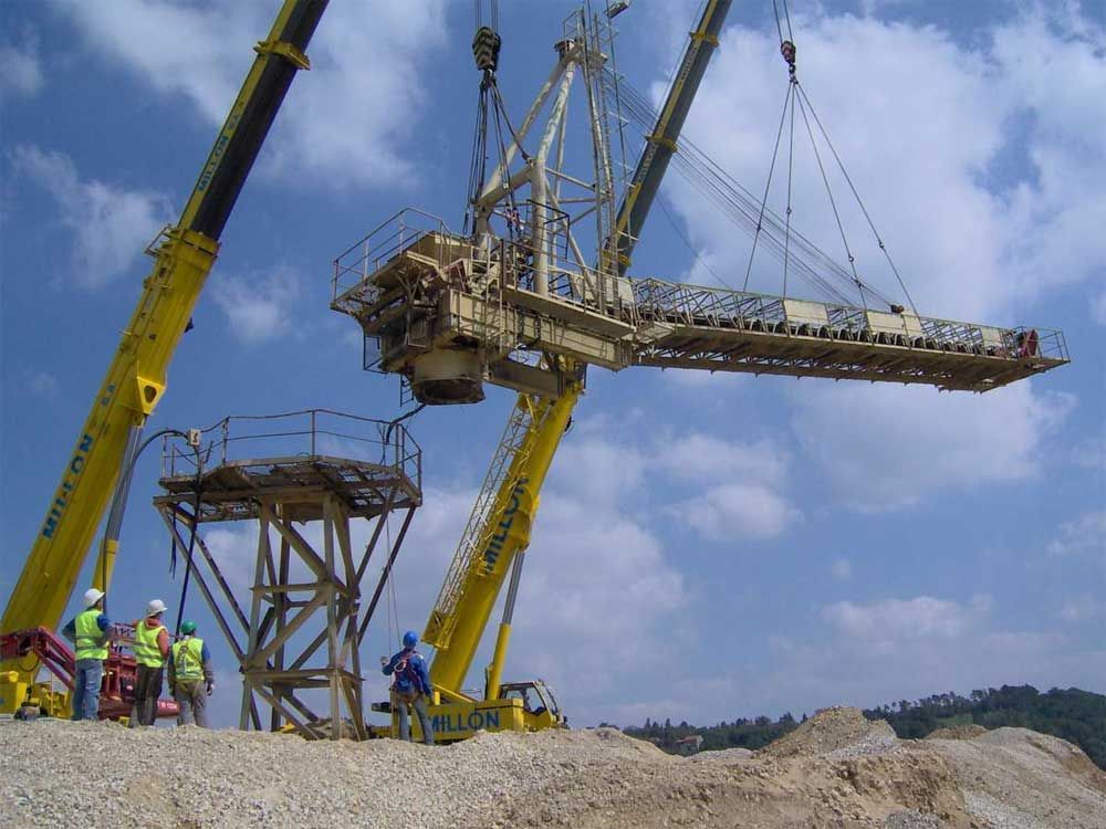 Deux grues jaunes soulèvent une grande structure industrielle au-dessus des ouvriers sur un chantier de construction.