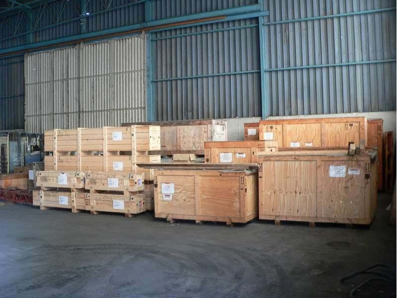 L'intérieur d'un entrepôt présente plusieurs grandes caisses d'expédition en bois disposées sur un sol en béton contre un mur métallique.