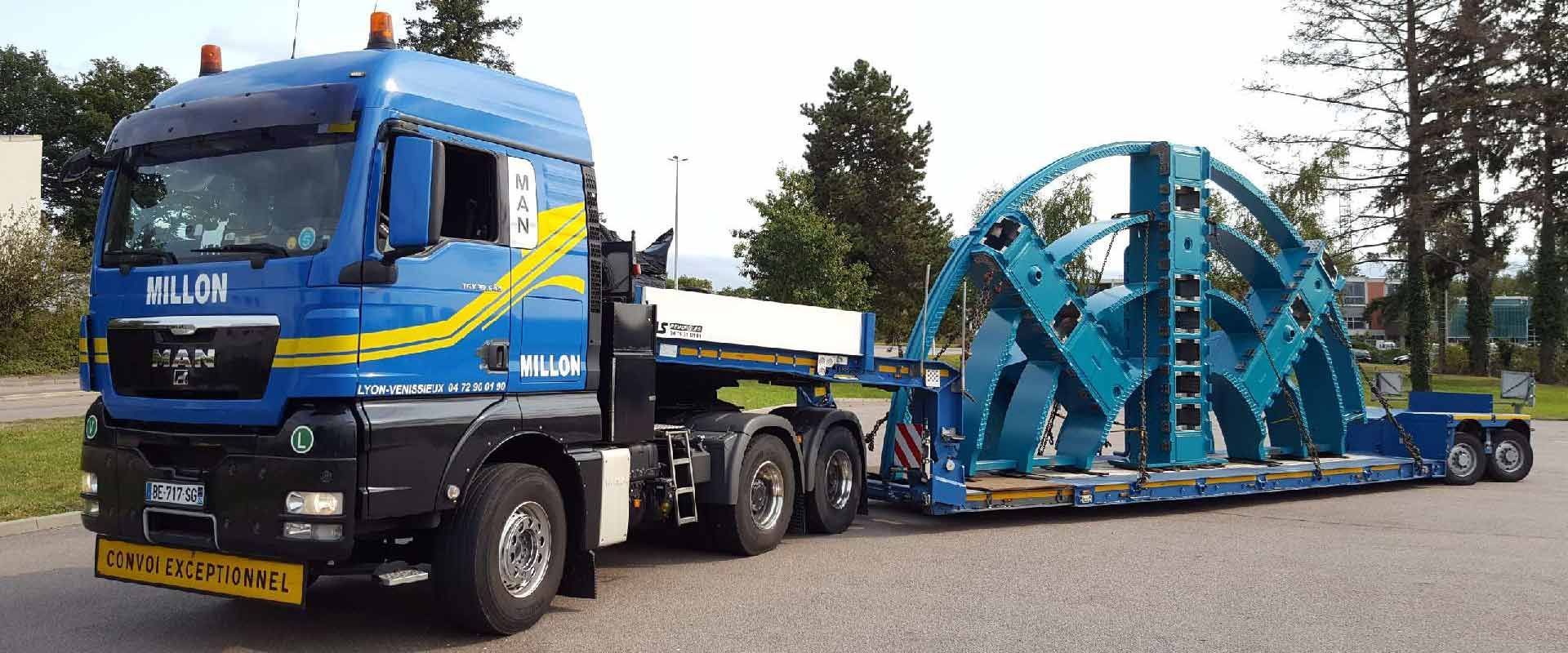 Un camion MAN bleu poids lourd transportant un grand composant industriel en acier arqué sur une remorque à plateau à l'extérieur.