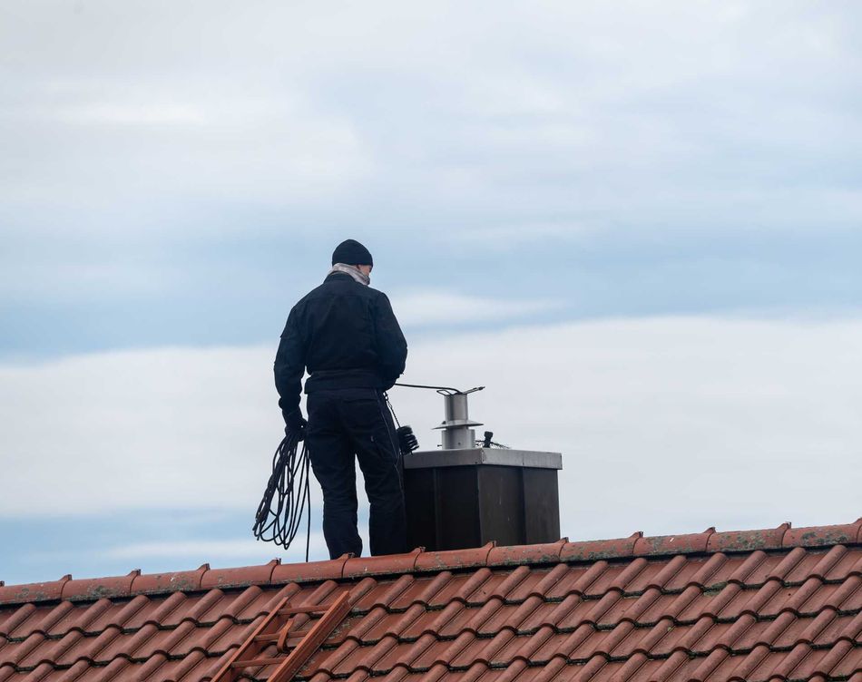 Un ramoneur sur le toit d’une maison en train de nettoyer un conduit de cheminée