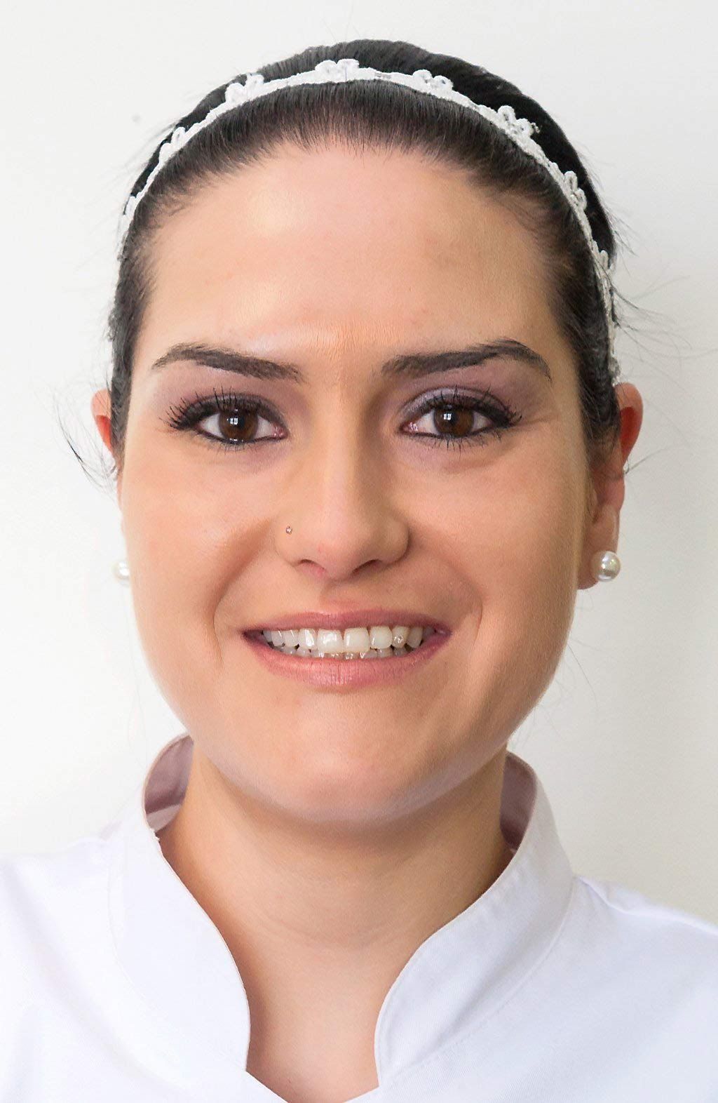 Primer plano de una persona con cabello oscuro recogido con una diadema blanca, sonriendo sobre un fondo blanco liso.