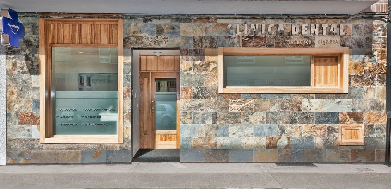 La fachada de una clínica dental, con revestimiento de piedra, puerta y ventanas con marcos de madera y el letrero "CLINIC DENTAL".