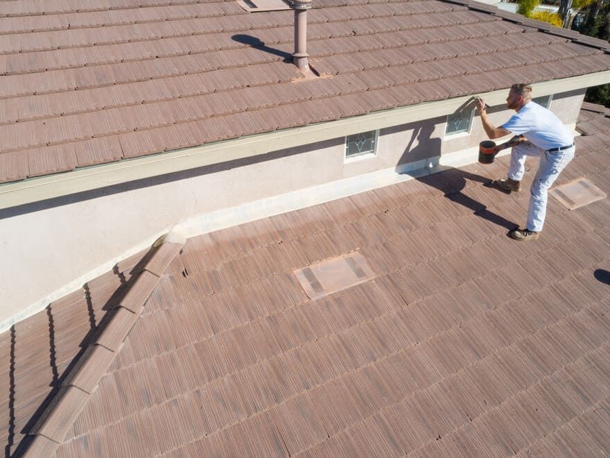 Un hombre está pintando el techo de una casa con un balde.