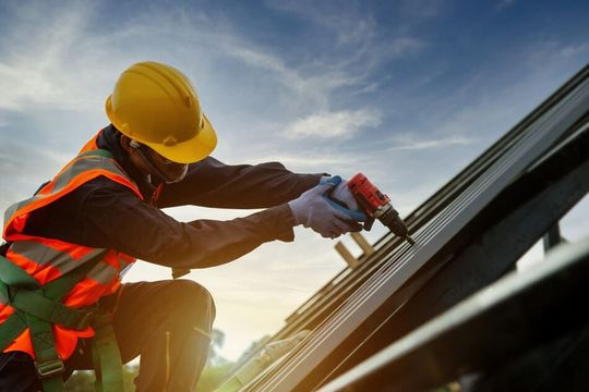 Un trabajador de la construcción está trabajando en un tejado con un taladro.
