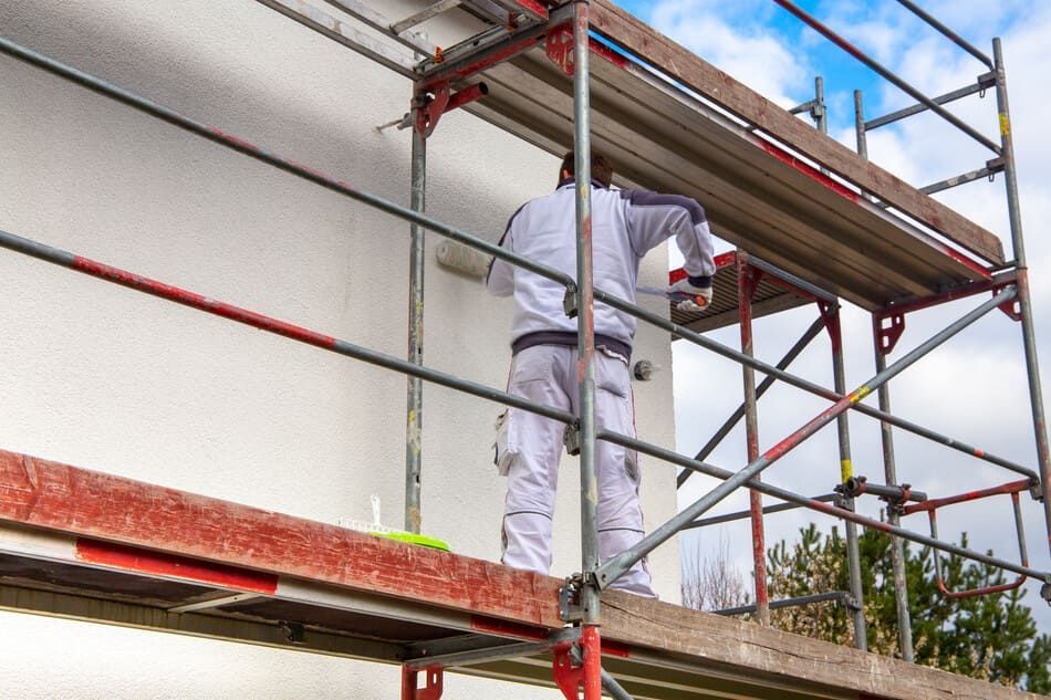 Un hombre está de pie en un andamio pintando un edificio.
