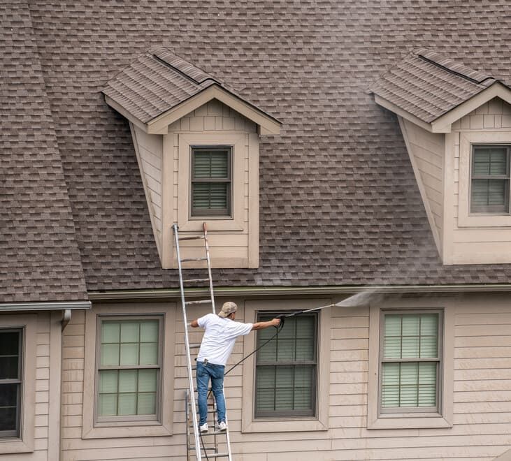 Un hombre en una escalera está limpiando el techo de una casa.