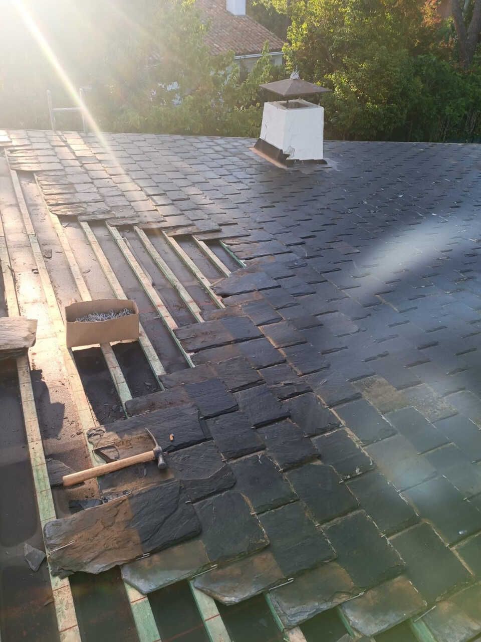Se está reparando un tejado con tejas de pizarra y una chimenea.