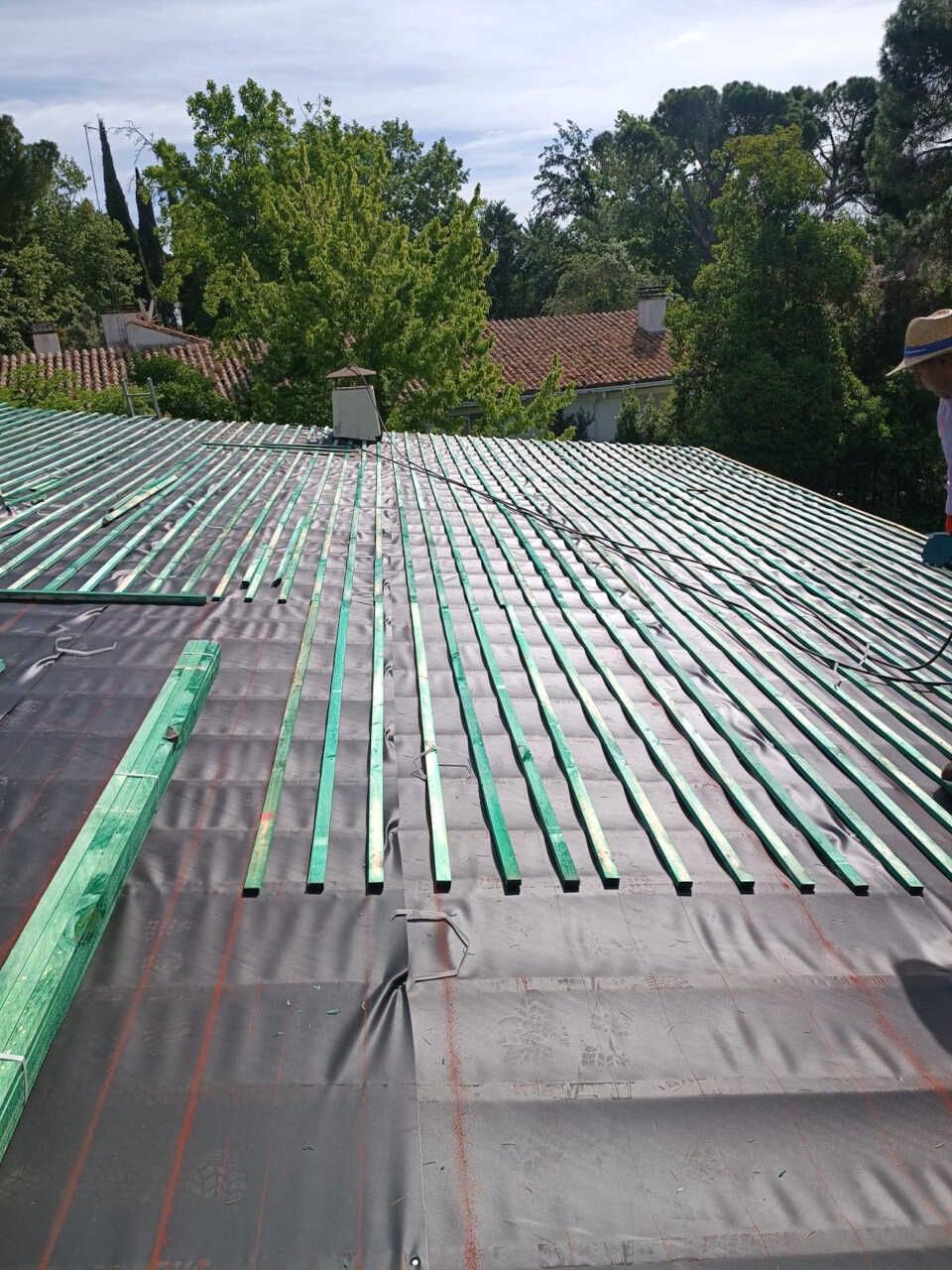 Un hombre con sombrero está parado sobre un tejado con rayas verdes.