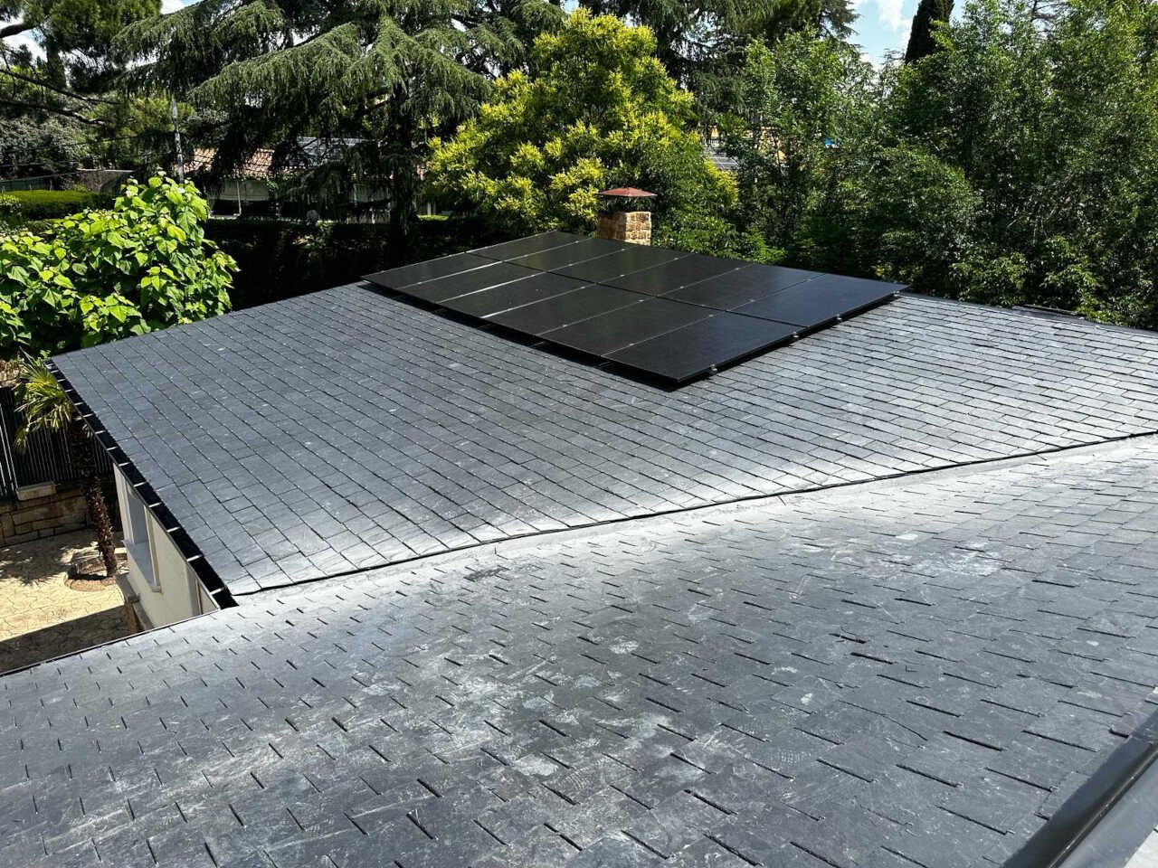 Un techo negro con paneles solares está rodeado de árboles.