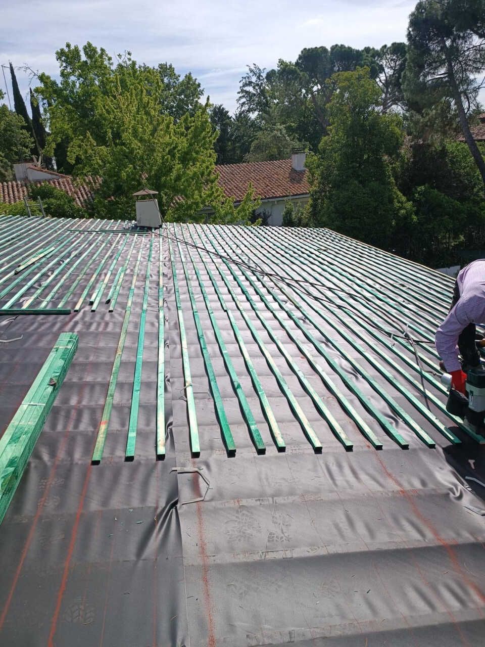 Un hombre está trabajando en un tejado con vigas verdes.