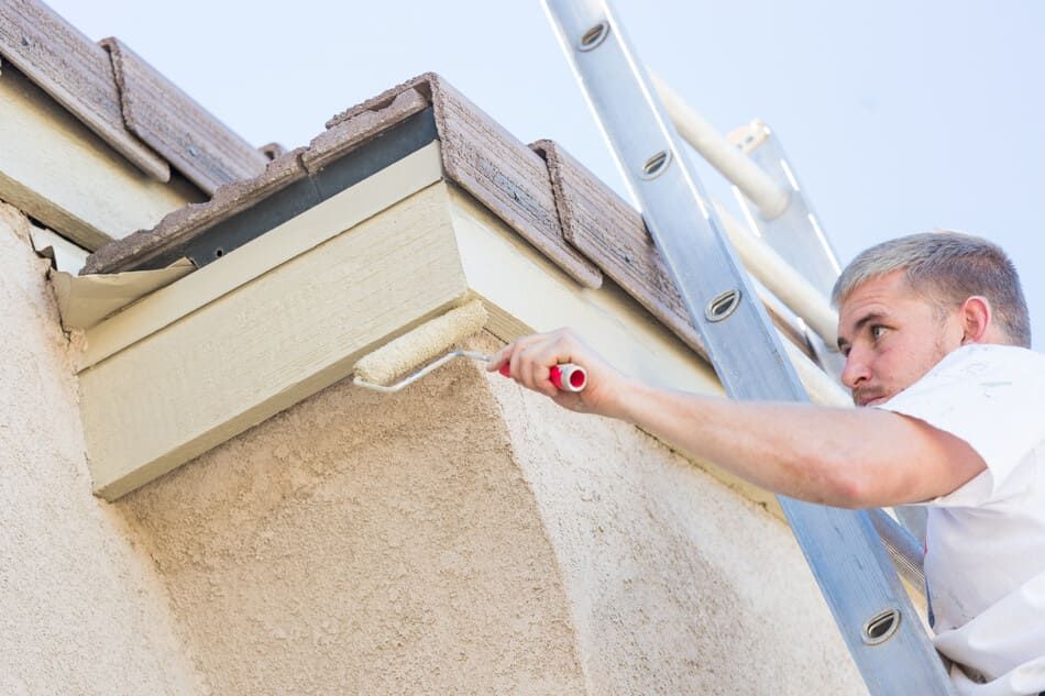 Un hombre está pintando una pared con un rodillo mientras está de pie en una escalera.