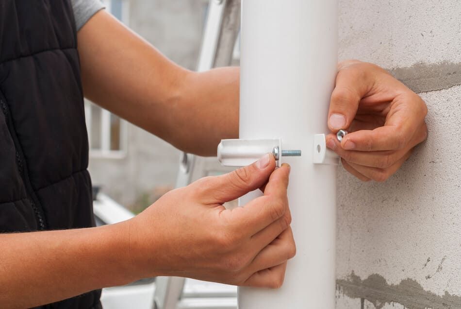 Una persona está instalando una canaleta para lluvia en una pared.