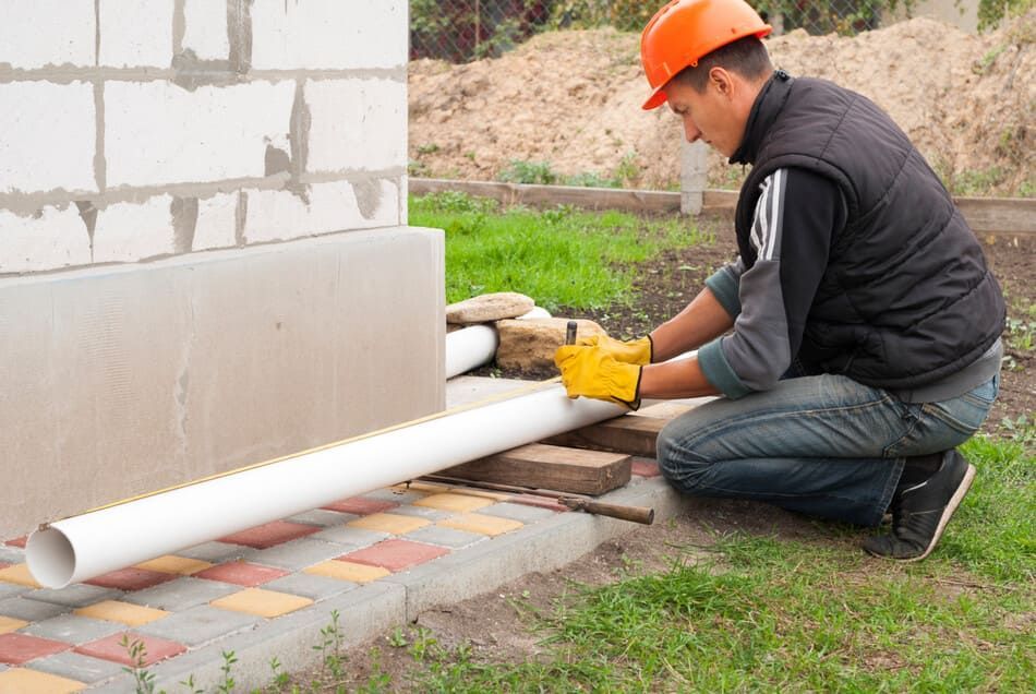 Un hombre que lleva un casco se arrodilla para instalar una tubería.