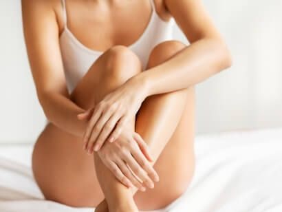 Una mujer está sentada en una cama con las piernas cruzadas y las manos sobre las piernas.