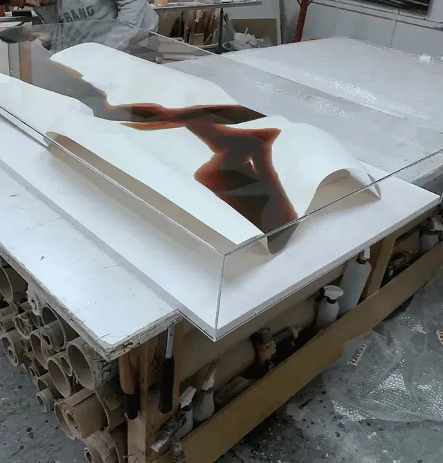 Escultura blanca con líquido oscuro vertido en ella, sobre una mesa blanca en un entorno de taller.