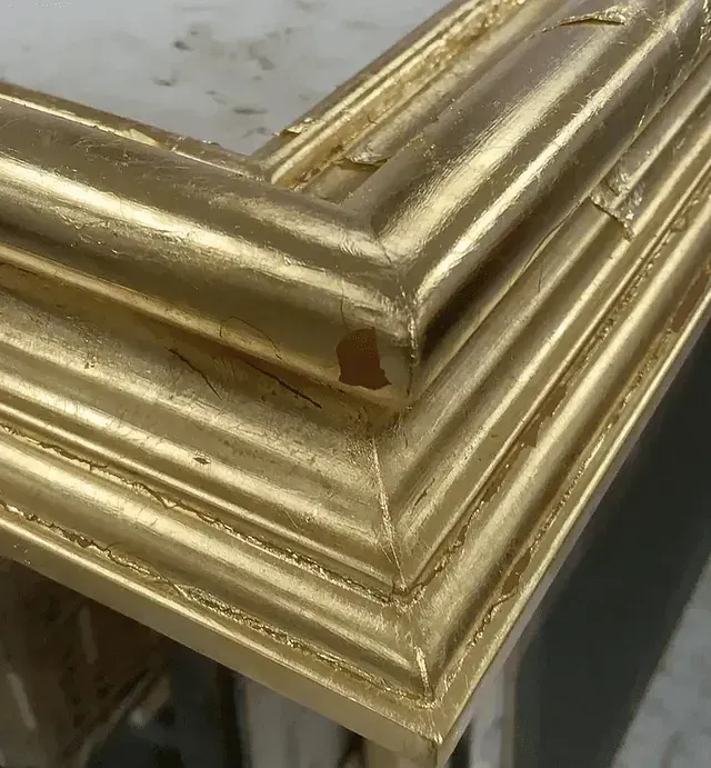 Primer plano de una esquina de un marco dorado con pequeños desprendimientos y desgaste.