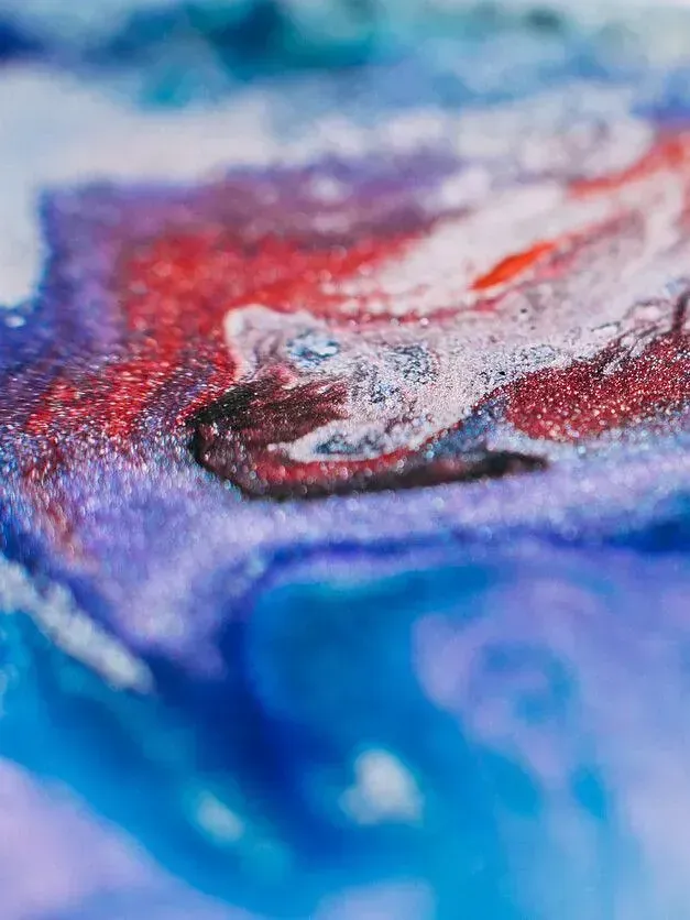 Obra de arte abstracta: remolinos de pintura líquida de color rojo, azul y violeta que crean un efecto texturizado y jaspeado.