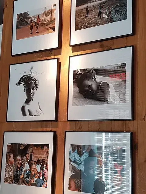 Seis fotografías enmarcadas sobre una pared de madera. Retratos y escenas de personas en blanco y negro.