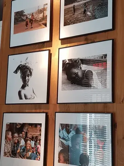 Seis fotografías enmarcadas sobre una pared de madera. Retratos y escenas de personas en blanco y negro.