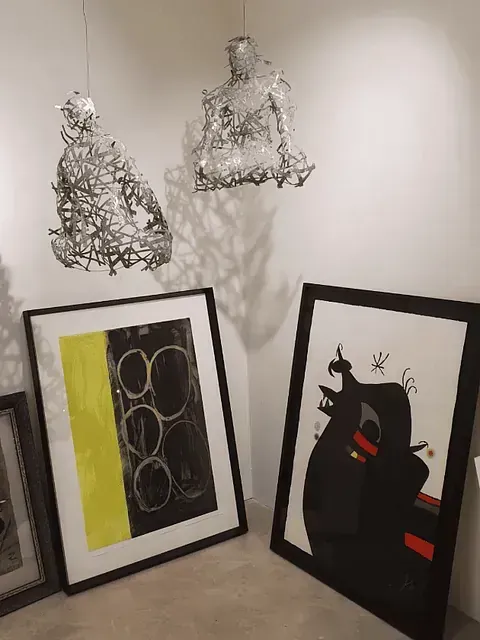 Esculturas de figuras de alambre cuelgan sobre arte enmarcado con diseños abstractos y una silueta de toro negro.