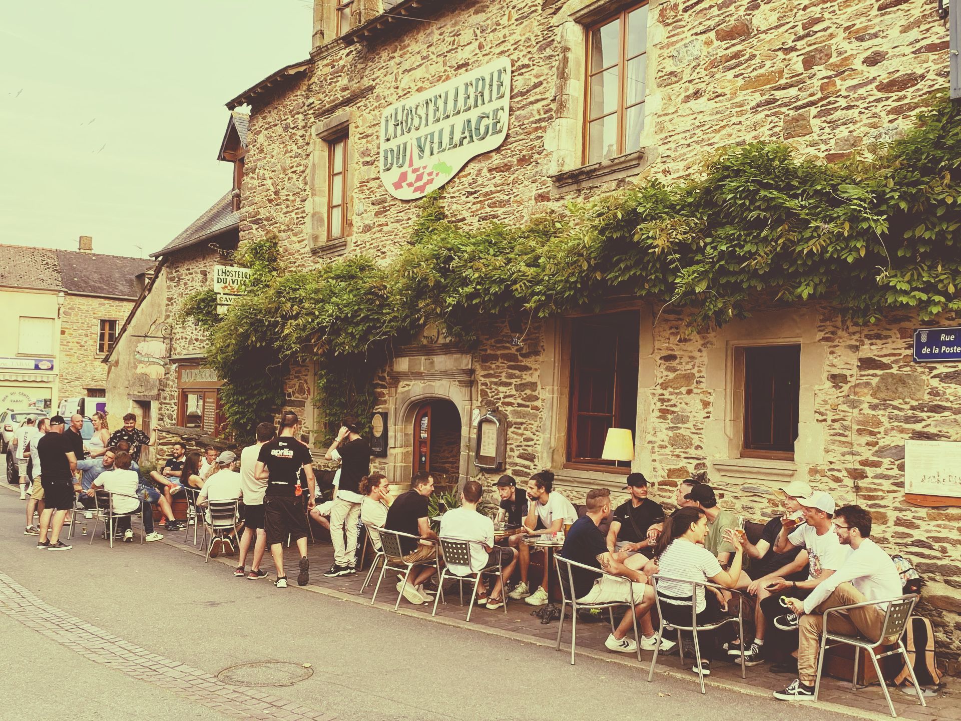 Devanture de l'établissement du Café du Village avec des gens en terrasse.