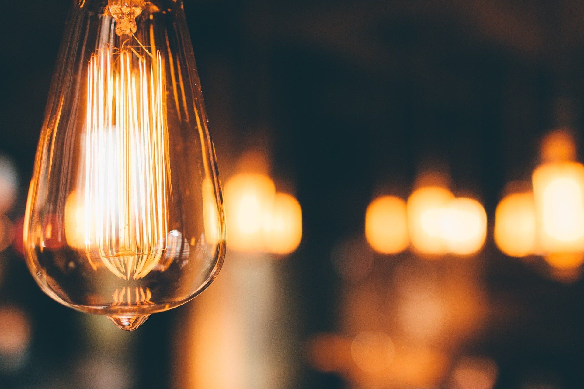 Gros plan sur une ampoule allumée de style Edison, avec des ampoules à lumière chaude floues en arrière-plan