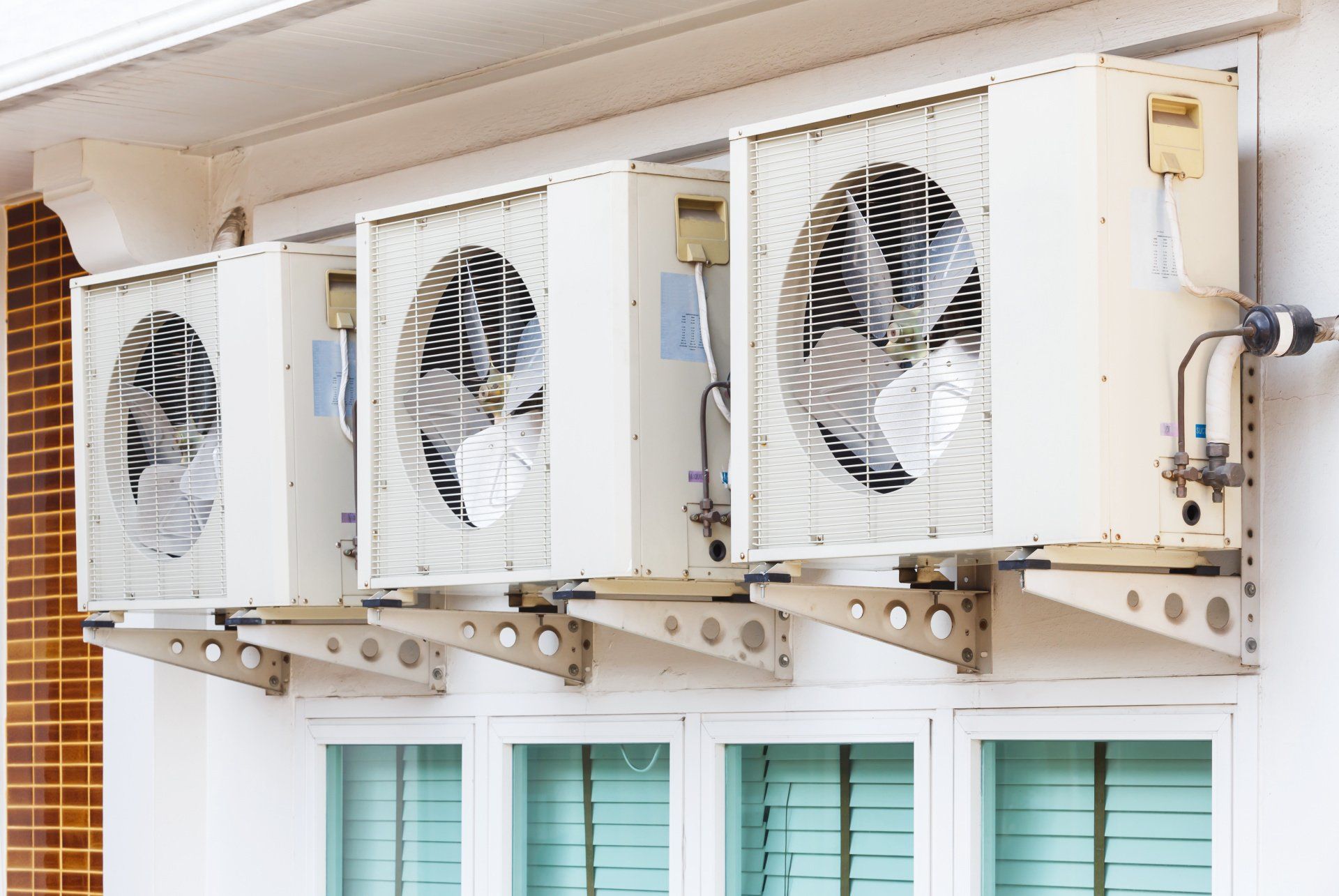 Unités de climatisation fixées sur un mur blanc d'un bâtiment, au-dessus de fenêtres avec des stores fermés