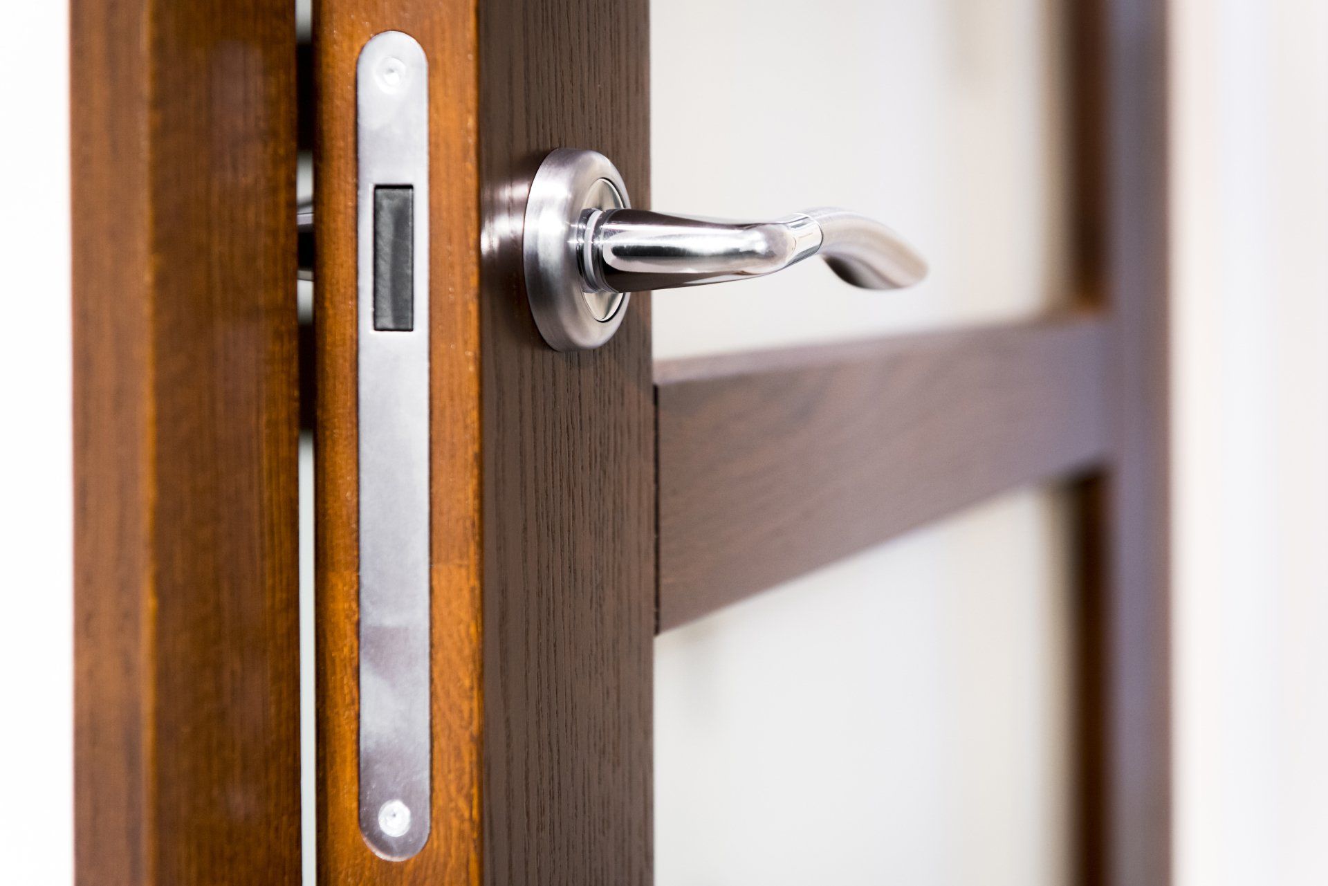 Porte avec une poignée chromée et un loquet argenté, sur un cadre en bois foncé