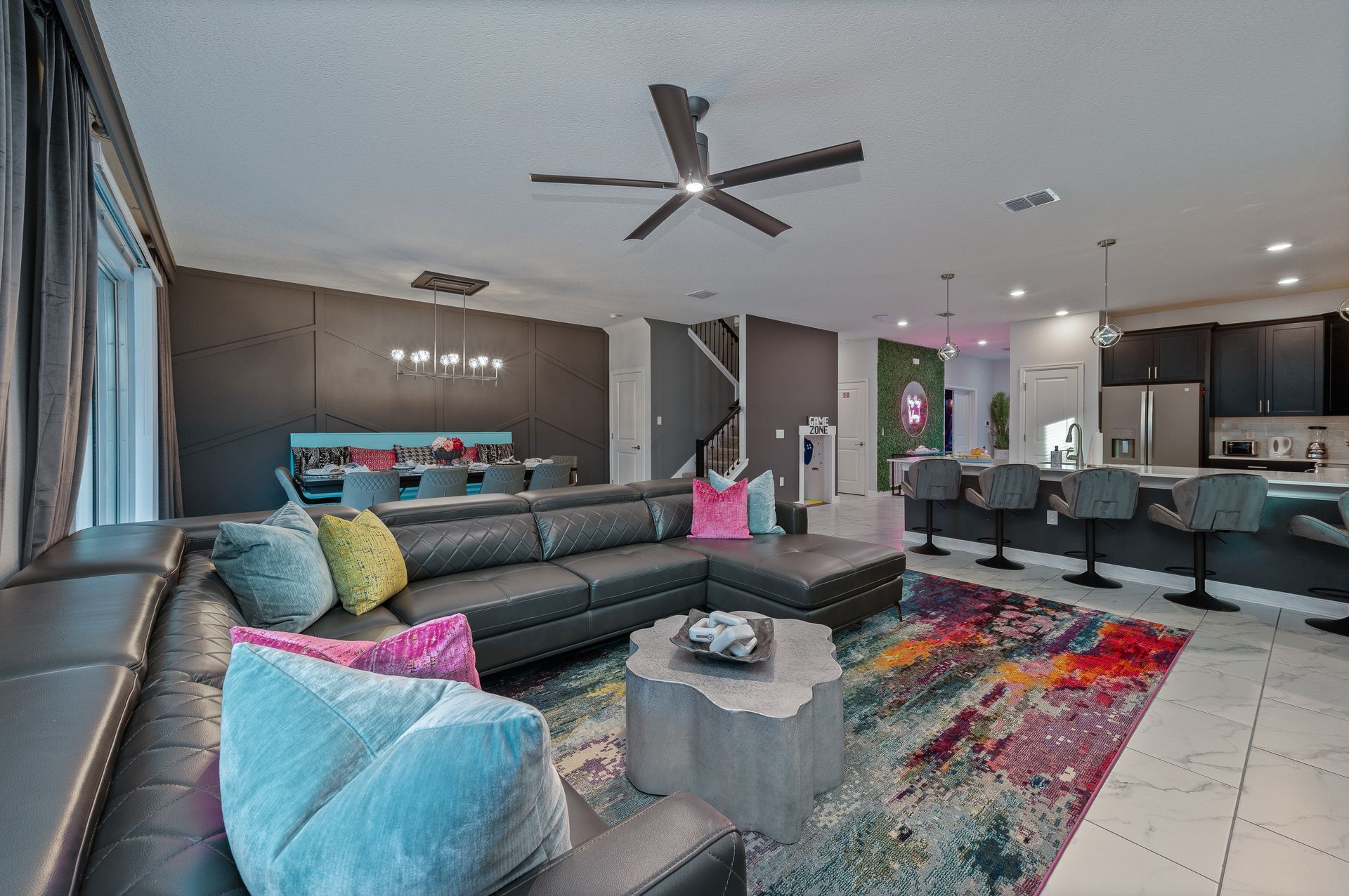 Spacious living room with dark leather sectional, colorful rug, and open kitchen with bar seating.