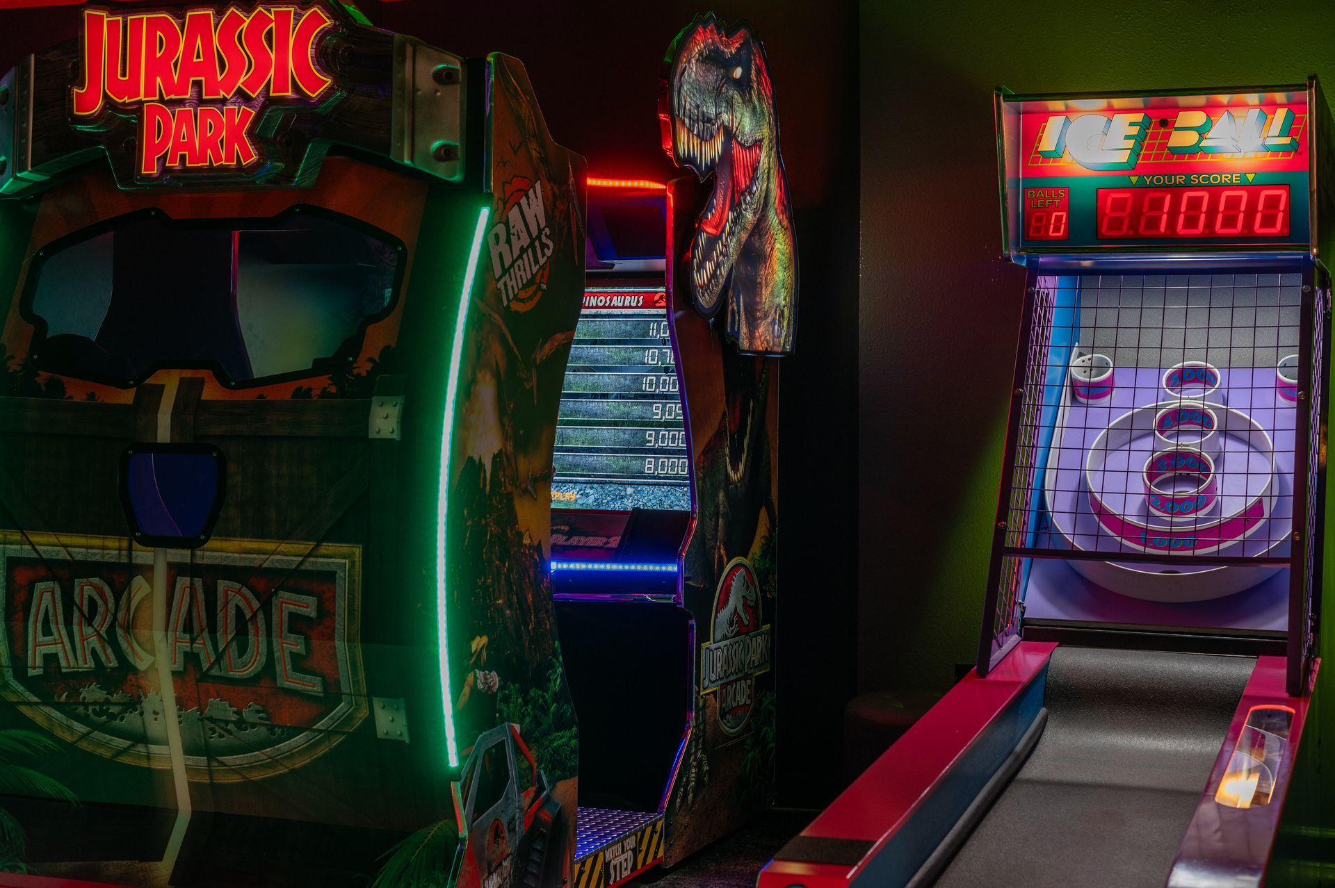 Arcade games in a dark room: Jurassic Park, a tall game with neon lights, and a Skee-Ball machine.