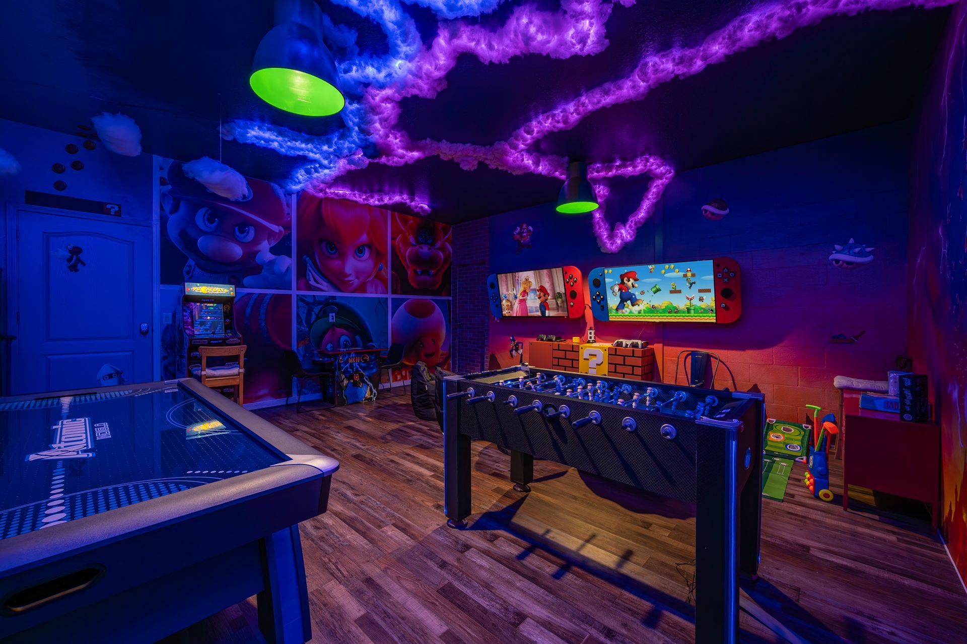 Game room with neon-lit ceiling, foosball, air hockey, arcade game, and multiple TVs for gaming.